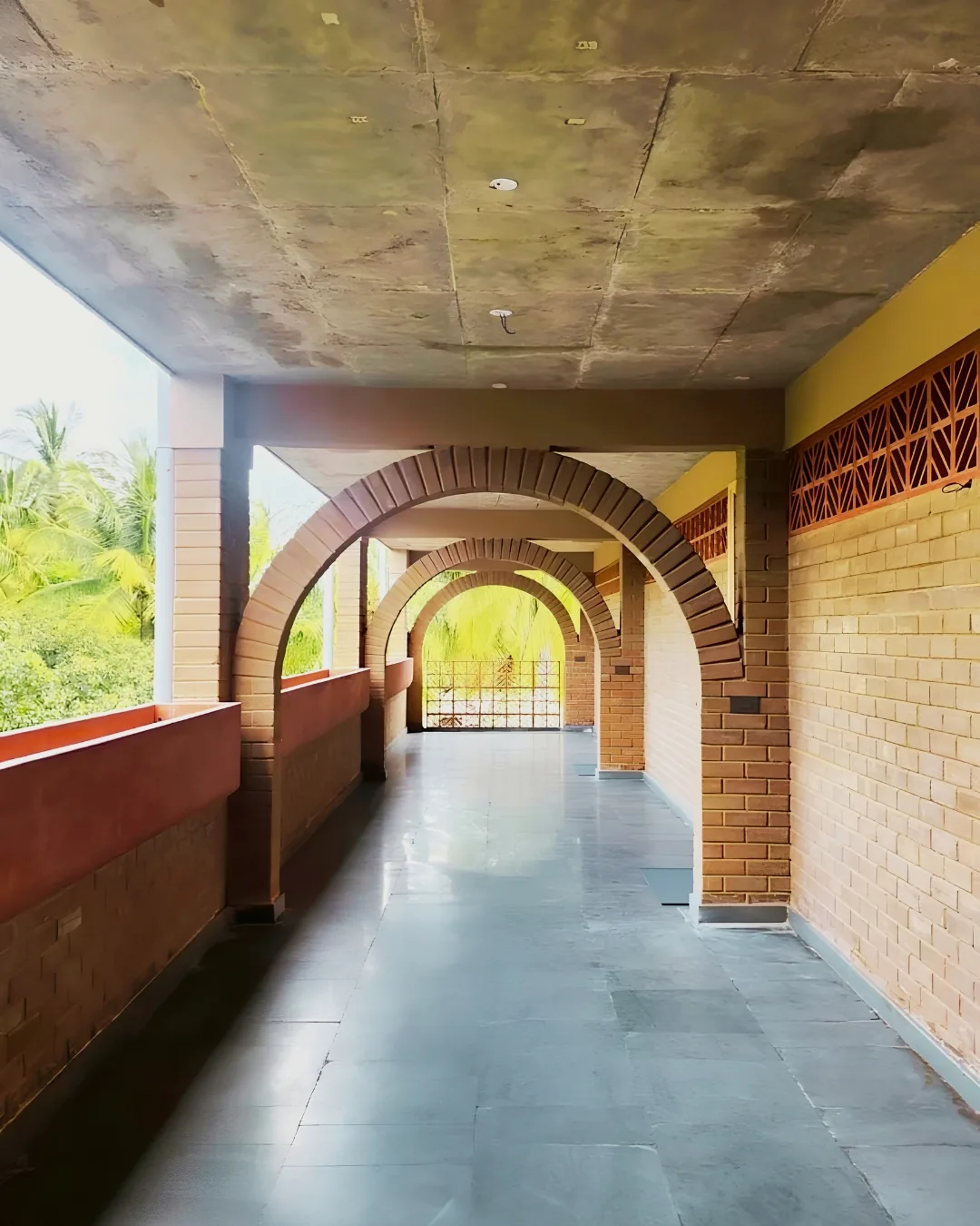 A run of earth-block arches along an open walkway, palms beyond the opening